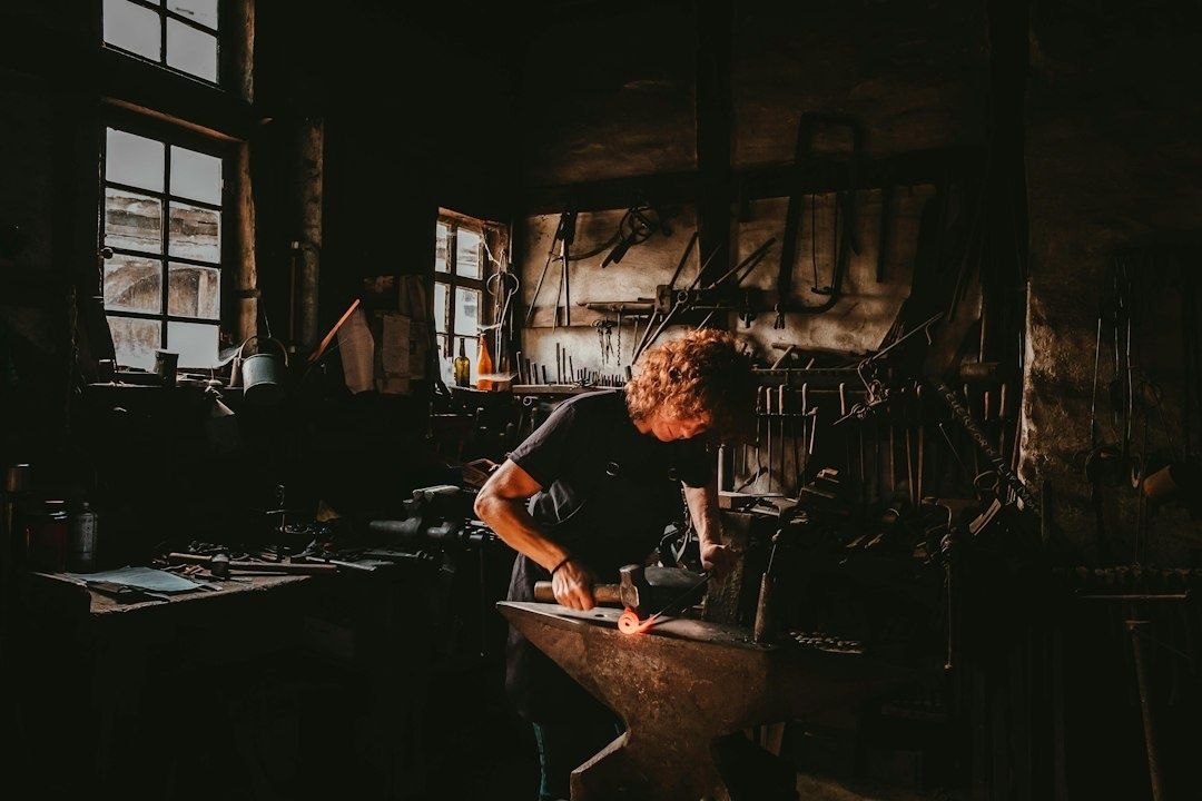 Artisan travaillant le métal au marteau dans une forge sombre